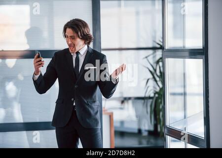 Using the phone. Portrait of handsome young businessman in black suit and tie Stock Photo