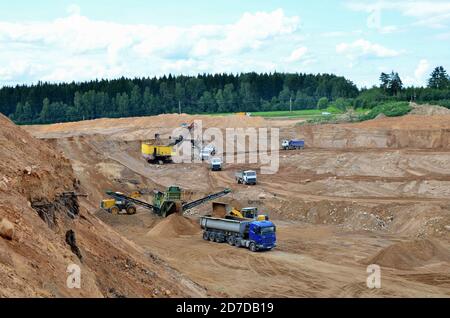Wheel front-end loader loads sand into a dump truck. Heavy machinery in the mining quarry, excavators and trucks. Mobile jaw crusher plant with belt c Stock Photo