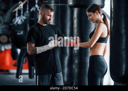 Wearing bandages. Young tattooed boxing coach teaches young woman in the gym Stock Photo