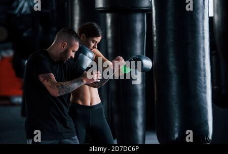 Young tattooed boxing coach teaches young woman in the gym