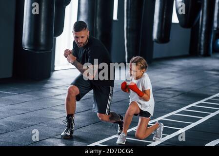 Basic punches. Young tattooed boxing coach teaches cute little girl in the gym Stock Photo