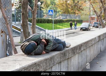 Poor homeless man or refugee sleeping on the street in the city. Problems of urban life in big modern cities, social documentary concept, selective Stock Photo