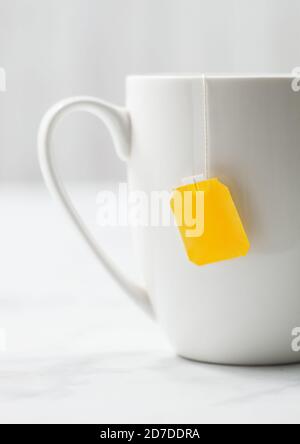 Teabag with yellow blank tag of black tea in white porcelain cup on white background. Stock Photo