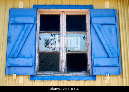 old blue window with open coverings on yellow wall Stock Photo