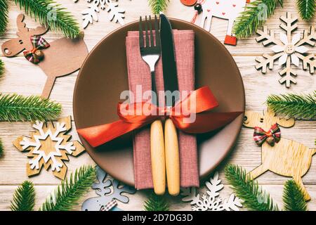 Top view of cutlery and plate on festive wooden background. New Year family dinner concept. Fir tree and Christmas decorations. Stock Photo