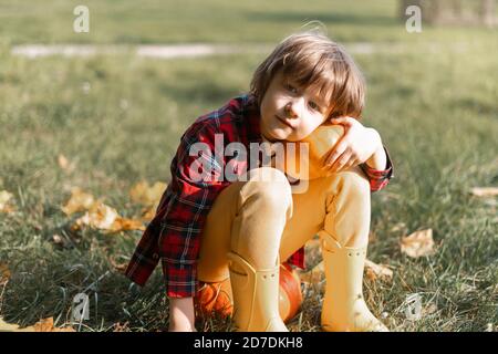 Cute boy play with pumpkin in autumn park on Halloween. Kids trick or treat. Fun in fall. Dressed up child. Stock Photo