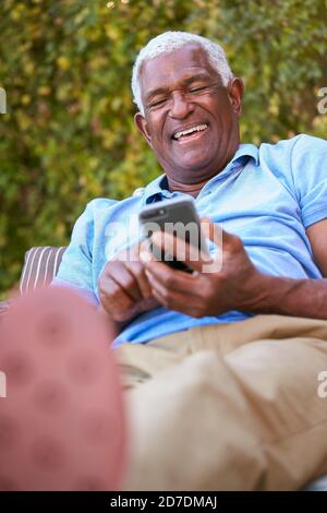 Smiling Senior African American Man Using Mobile Phone Sitting Outdoors In Garden At Home Stock Photo