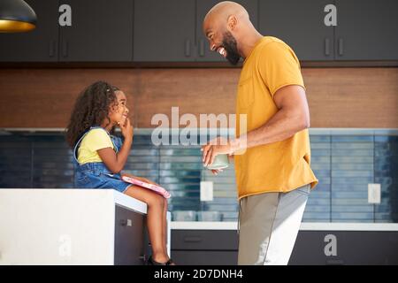 Father With Daughter Sitting On Kitchen Counter At Home Using Digital Tablet Stock Photo