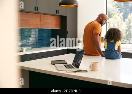 Father With Daughter Sitting On Kitchen Counter At Home Using Digital Tablet Stock Photo