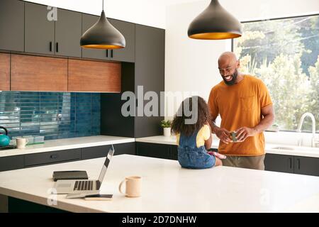 Father With Daughter Sitting On Kitchen Counter At Home Using Digital Tablet Stock Photo