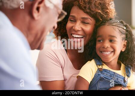 Close up Of Loving Grandparents Cuddling Granddaughter At Home Stock Photo