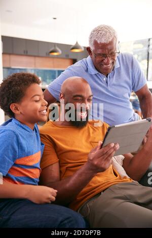 Multi-Generation Male African American Family Sitting On Sofa At Home Using Digital Tablet Stock Photo