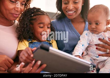 Multi-Generation Female African American Family Sitting On Sofa At Home Using Digital Tablet Stock Photo