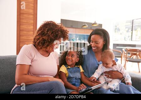 Multi-Generation Female African American Family Sitting On Sofa At Home Using Digital Tablet Stock Photo