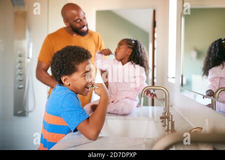 Father Helping Children To Brush Teeth In Bathroom At Home Stock Photo