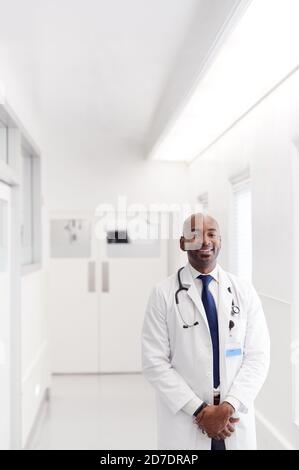 Portrait Of Mature Male Doctor Wearing White Coat Standing In Hospital Corridor Stock Photo