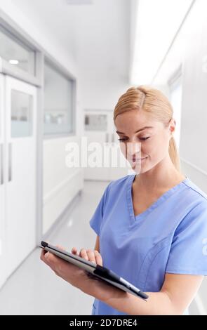 Female Doctor Wearing Scrubs In Hospital Corridor Using Digital Tablet Stock Photo