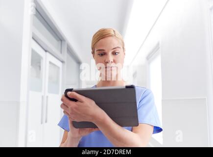 Female Doctor Wearing Scrubs In Hospital Corridor Using Digital Tablet Stock Photo