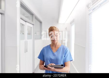 Female Doctor Wearing Scrubs In Hospital Corridor Using Digital Tablet Stock Photo