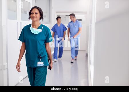 Female Doctor Wearing Scrubs In Hospital Walking Along Corridor Holding Digital Tablet Stock Photo