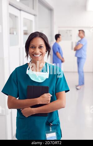 Portrait Of Smiling Female Doctor Wearing Scrubs In Hospital Corridor Holding Digital Tablet Stock Photo