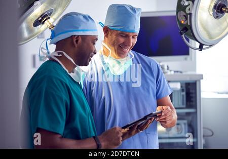 Male Surgeons Wearing Scrubs Looking At Digital Tablet In Hospital Operating Theater Stock Photo