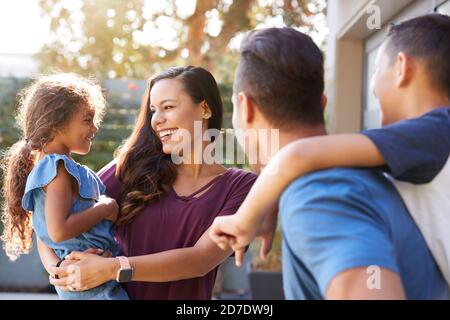 Smiling Hispanic Family With Parents Giving Children Piggyback Rides In Garden At Home Stock Photo