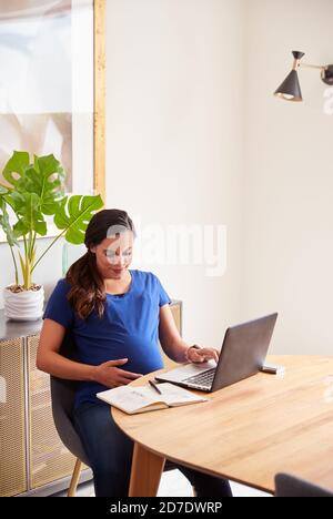 Pregnant Woman Using Laptop At Table Working From Home Stock Photo