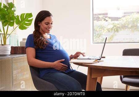 Pregnant Woman Using Laptop At Table Working From Home Stock Photo