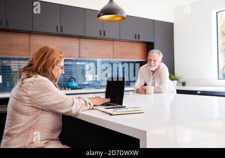 Senior Hispanic Couple At Home Sitting At Kitchen Island Using Laptop And Drinking Coffee Stock Photo