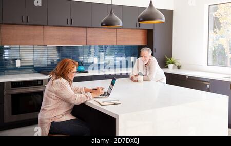 Senior Hispanic Couple At Home Sitting At Kitchen Island Using Laptop And Drinking Coffee Stock Photo