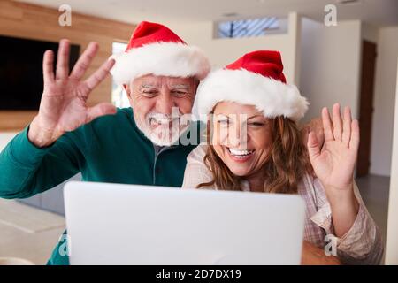 Senior Hispanic Couple Wearing Santa Hats With Laptop Having Video Chat With Family At Christmas Stock Photo