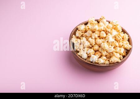 Popcorn with caramel in wooden bowl on a pastel pink background. Side view, copy space. Stock Photo