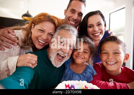 Multi-Generation Hispanic Family Taking Selfie To Celebrate Granddaughters Birthday At Home Stock Photo