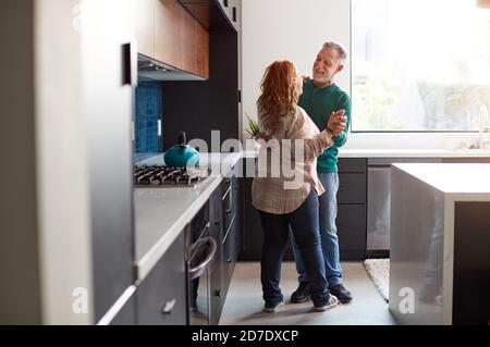 Senior Hispanic Couple At Home Dancing In Kitchen Together Stock Photo