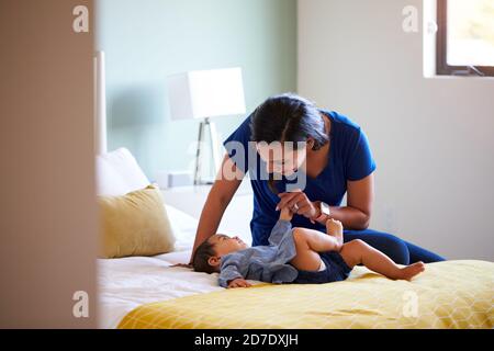 Mother Playing With Baby Daughter Lying On Bed At Home Stock Photo