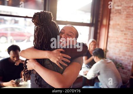 Female Friends Greeting Each Other With Hug As They Meet In Coffee Shop Stock Photo