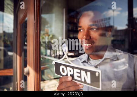 Male Owner Of Start Up Coffee Shop Or Restaurant Turning Round Open Sign On Door Stock Photo