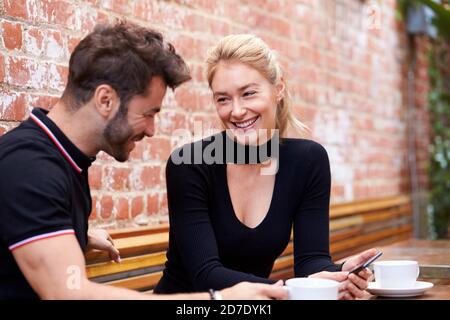 Young Couple On Date Sitting At Outdoor Coffee Shop Table Together Stock Photo