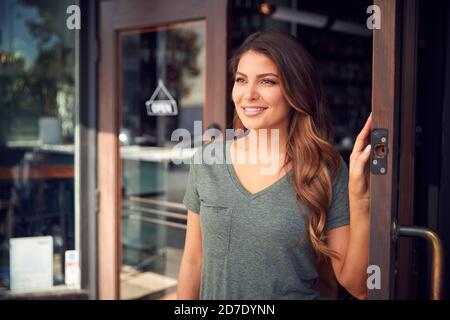 Female Owner Of Start Up Coffee Shop Or Restaurant Standing In Doorway Stock Photo