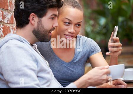 Young Couple On Date Taking Selfie On Mobile Phone Sitting At Outdoor Coffee Shop Table Together Stock Photo