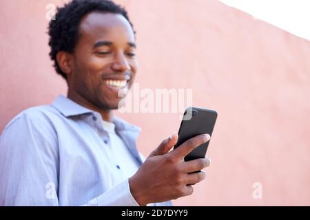 Outdoor Portrait Of Man Using Mobile Phone In The Street Leaning Against Wall Stock Photo
