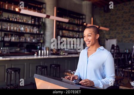 Female Owner Of Restaurant Bar Standing At Counter Using Digital Tablet Stock Photo