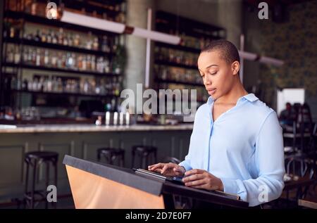 Female Owner Of Restaurant Bar Standing At Counter Using Digital Tablet Stock Photo