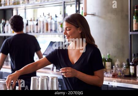 Female Bartender Mixing Ingredients For Cocktail Behind Bar Stock Photo