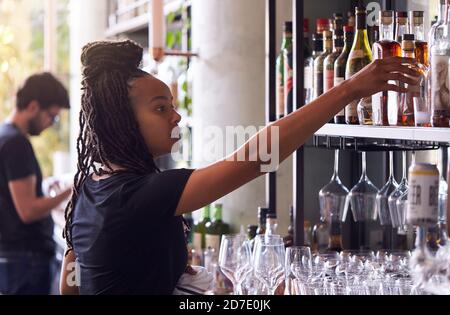 Female Bartender Arranging Bottles Of Alcohol Behind Bar Stock Photo