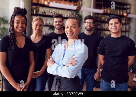 Portrait Of Female Owner Of Restaurant Bar With Team Of Waiting Staff Standing By Counter Stock Photo