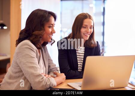 Two Businesswomen With Laptop Collaborating On Project In Office Together Stock Photo