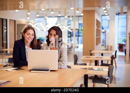 Two Businesswomen With Laptop At Desk In Open Plan Office Collaborating On Project Together Stock Photo