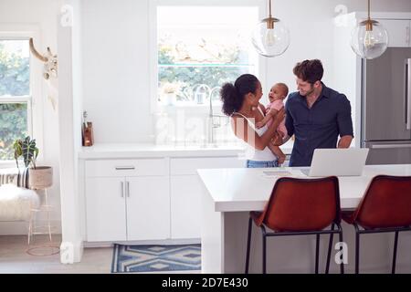 Family With Baby Daughter In Kitchen Using Laptop On Counter Stock Photo